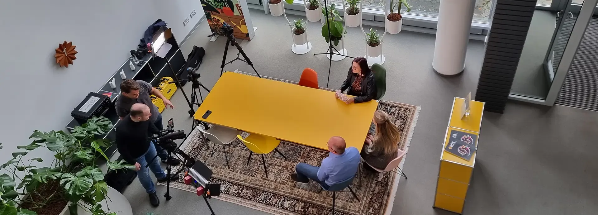 Blick von oben auf ein Fernsehinterview an einem gelben Tisch mit Kamerateam