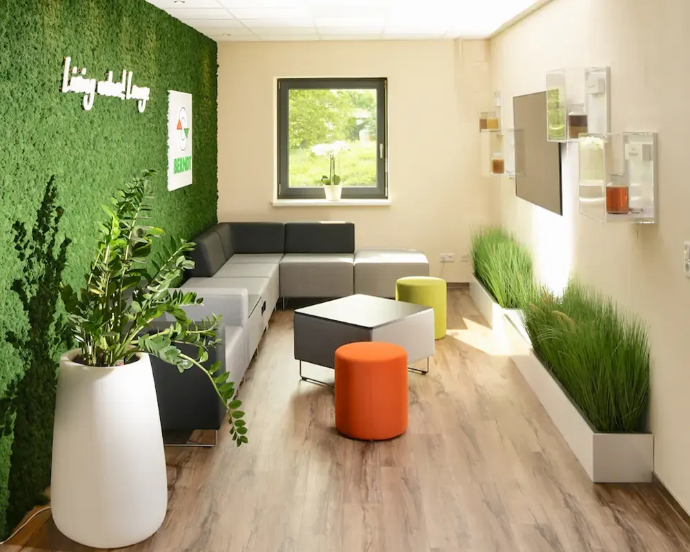 Loungebereich mit Mooswand, Polstermodulen und orangefarbenem Hocker