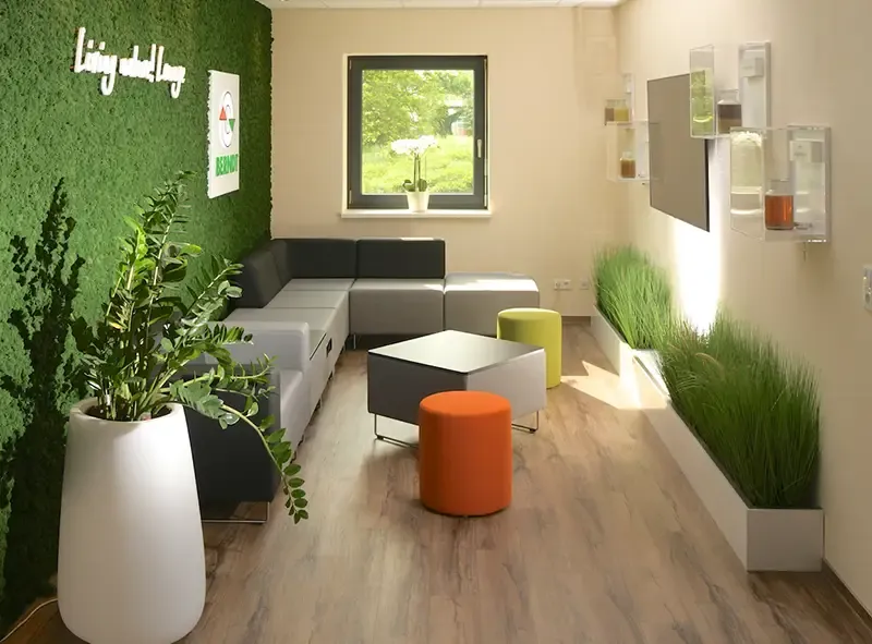 Loungebereich mit Mooswand, Polstermodulen, orangefarbenem Hocker und Gräsern