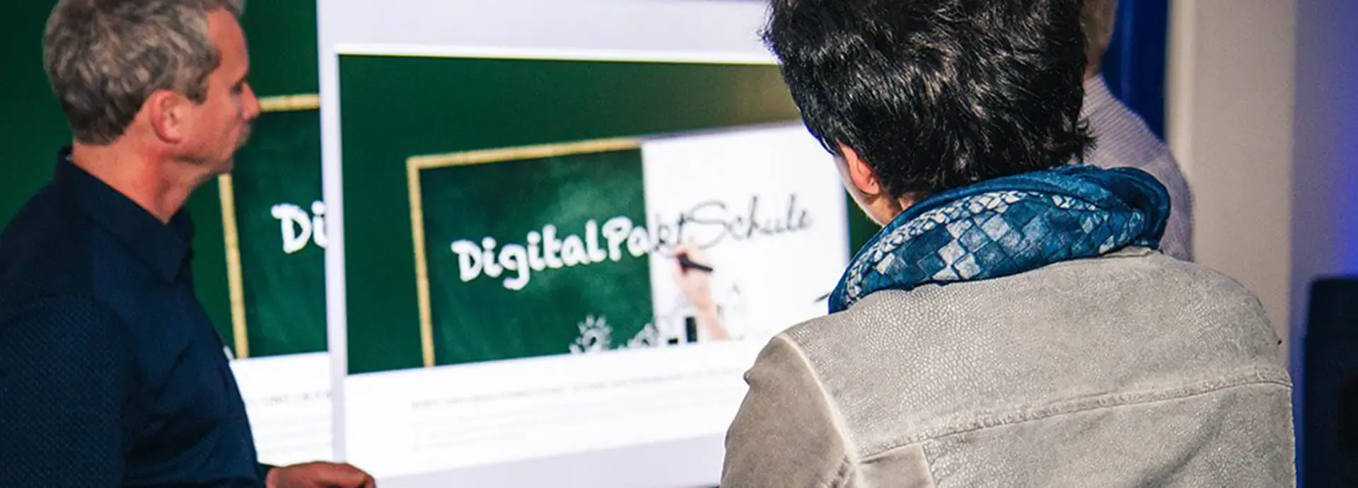Zwei Personen betrachten die Projektion der Seite „DigitalPakt Schule“