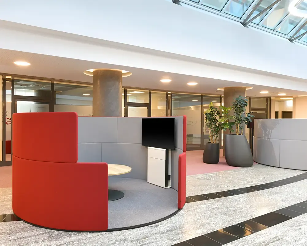 Runde Sitzinsel in Rot und Grau mit Bildschirm im Foyer