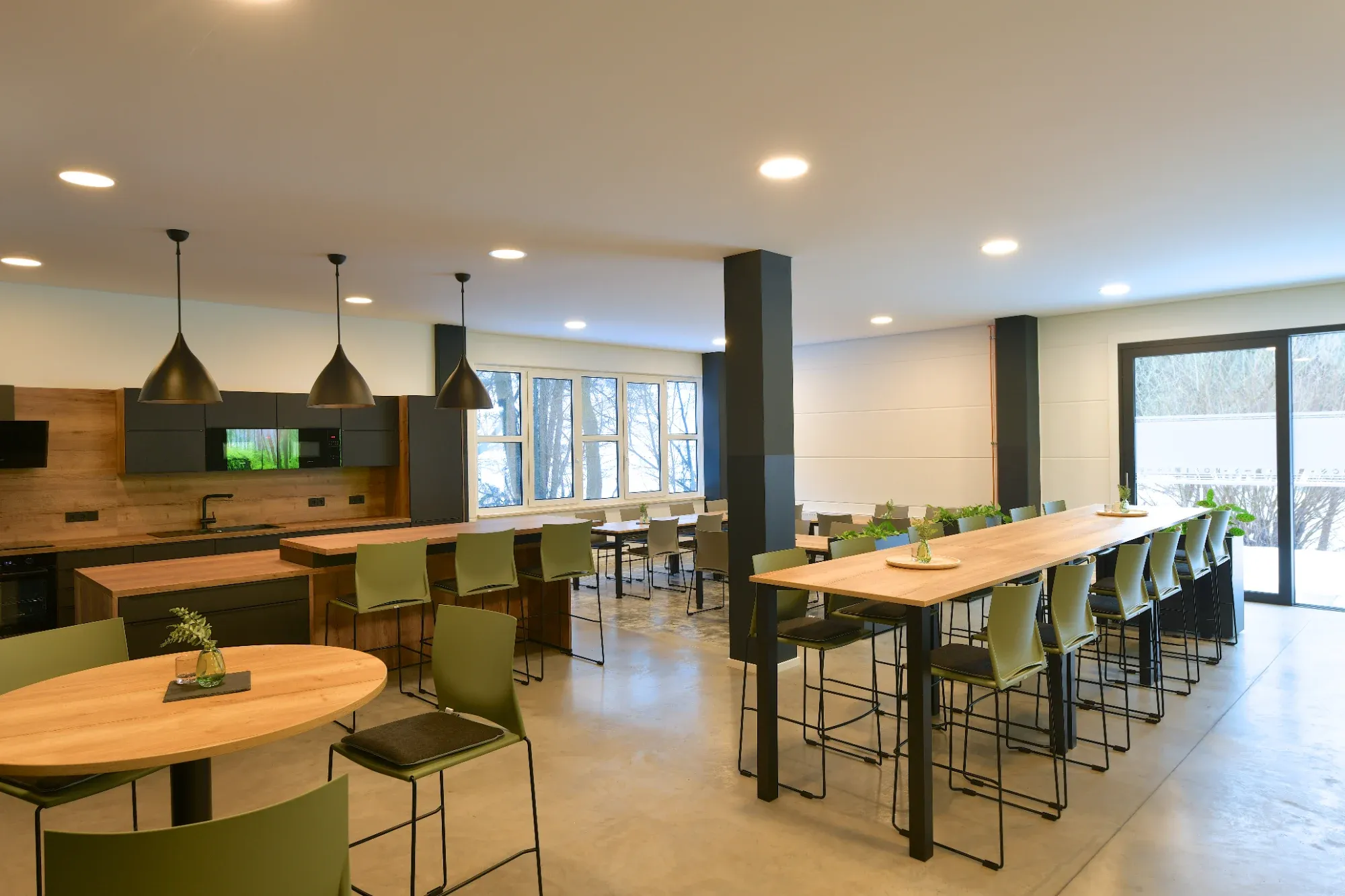 Kantine mit Holztischen, blaugrauen Stühlen und Leinwand vor einer Palettenwand