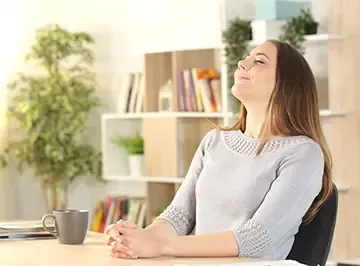 Frau am Schreibtisch lehnt sich entspannt zurück und atmet durch