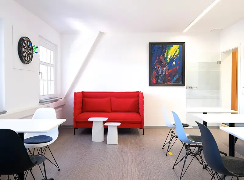 Aufenthaltsraum mit rotem Sofa, Beistelltischen und Sitzgruppen