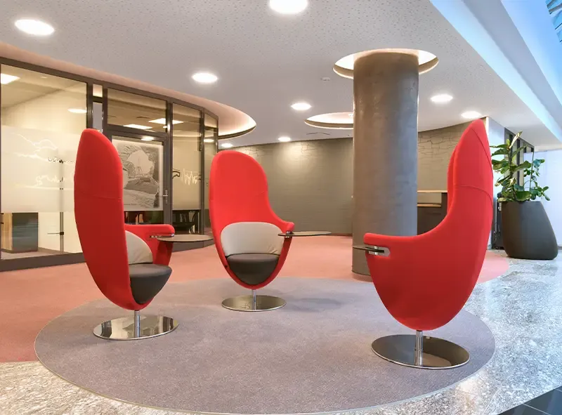 Drei rote Muschelsessel im Foyer neben einer Betonstütze