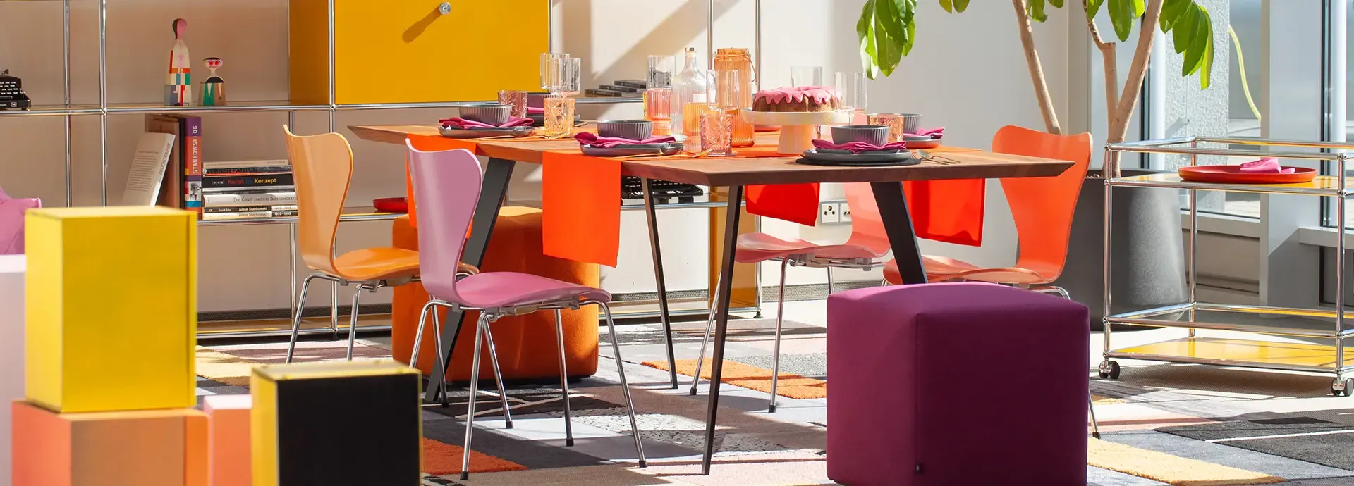Besprechungstisch mit orange-violetten Stühlen und Sitzwürfeln