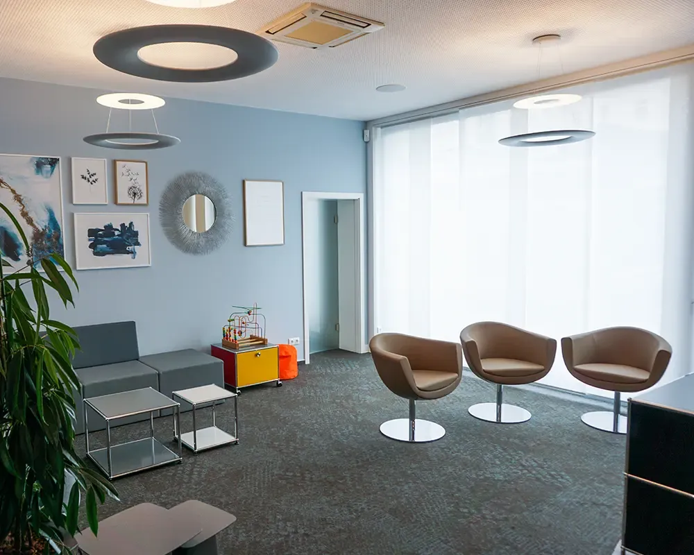Wartezimmer mit braunen Drehsesseln, Bilderwand und Deckenleuchten