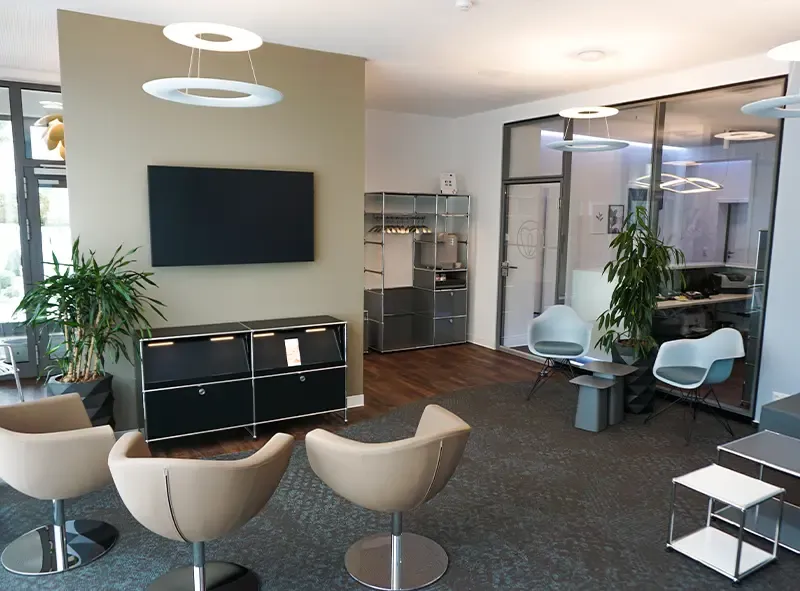 Wartebereich mit Bildschirm, schwarzem Sideboard und beigen Drehsesseln