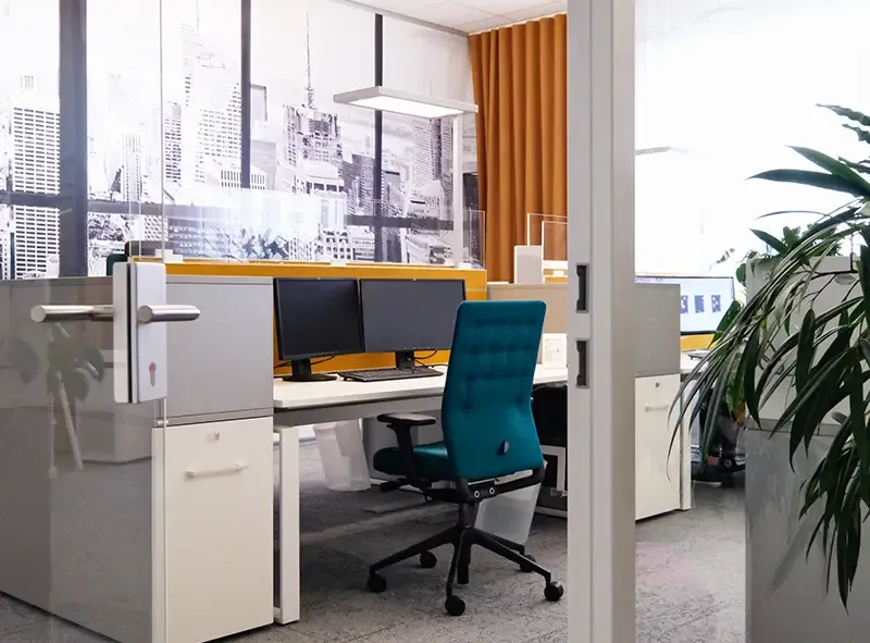 Arbeitsplätze mit gelben Trennwänden und blauem Drehstuhl hinter einer Glastür
