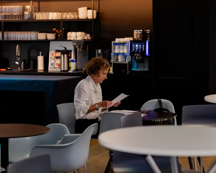 Frau liest Unterlagen an einem Tisch vor der Kaffeebar