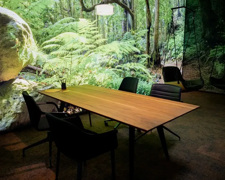 Besprechungstisch aus Holz vor einer Waldtapete, dahinter ein Hängesessel