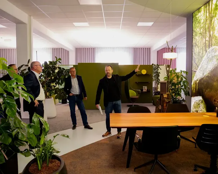 Besucher der Dialogveranstaltung im begrünten Büroraum, ein Redner zeigt zur Seite