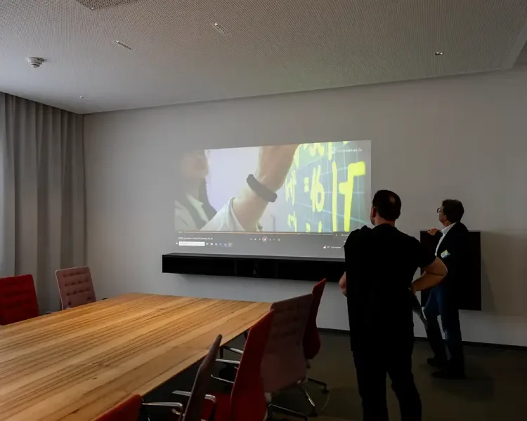 Zwei Männer vor einer großen Projektion im Besprechungsraum mit langem Holztisch