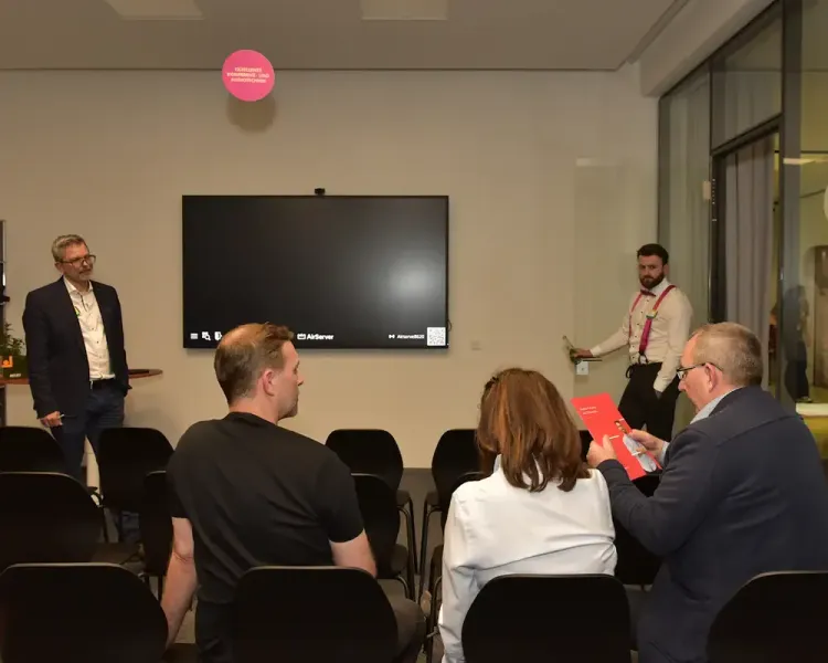 Vortrag vor kleiner Zuhörergruppe im Besprechungsraum mit Bildschirm
