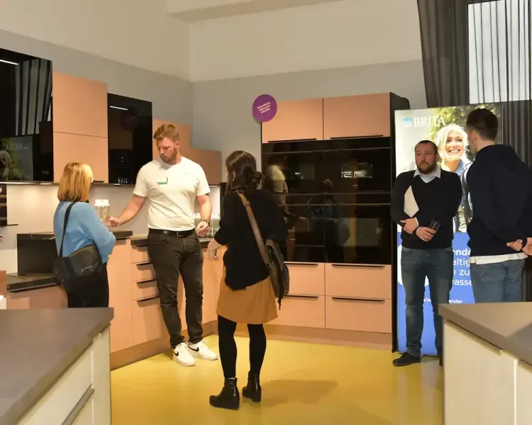 Gäste im Gespräch in der Küchenausstellung, rechts ein Rollup