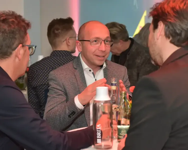 Gäste im Gespräch an einem Stehtisch mit Getränkeflasche