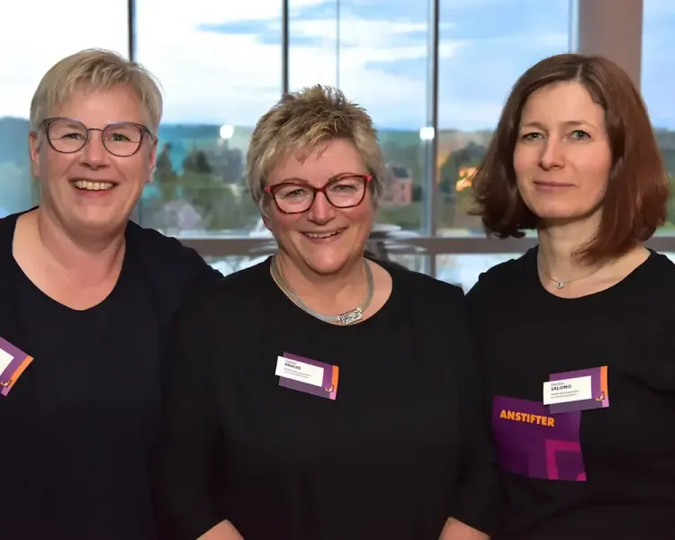 Drei Mitarbeiterinnen mit „Anstifter“-Shirts vor der Fensterfront