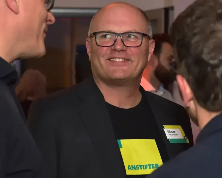 Besucher mit „Anstifter“-Shirt im Gespräch mit zwei Gästen