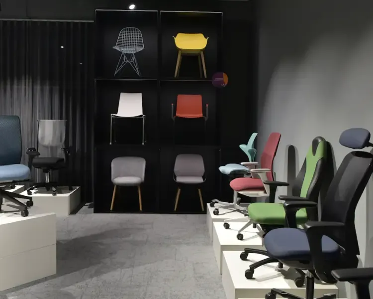 Ausstellung mit Bürodrehstühlen in Blau, Grün und Rot, dahinter eine Bilderwand mit Stuhlmodellen
