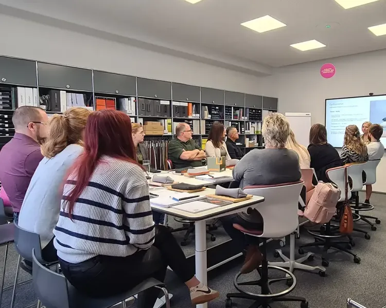 Teilnehmende am Konferenztisch, dahinter die Musterregale des Schulungsraums