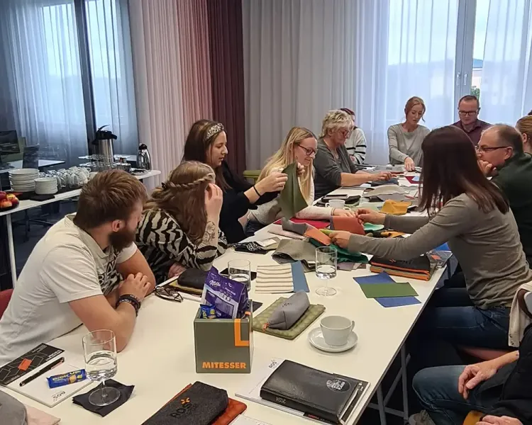Workshop-Teilnehmende begutachten Stoff- und Farbmuster an einer langen Tischreihe