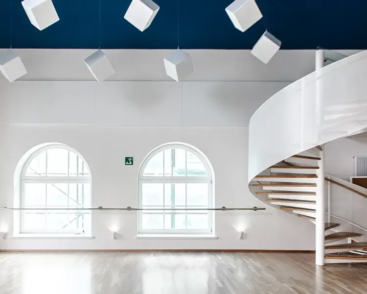 Weiße Akustikwürfel unter der Decke, rechts eine weiße Wendeltreppe