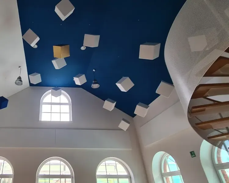 Blick nach oben auf die blaue Decke mit hängenden Akustikwürfeln