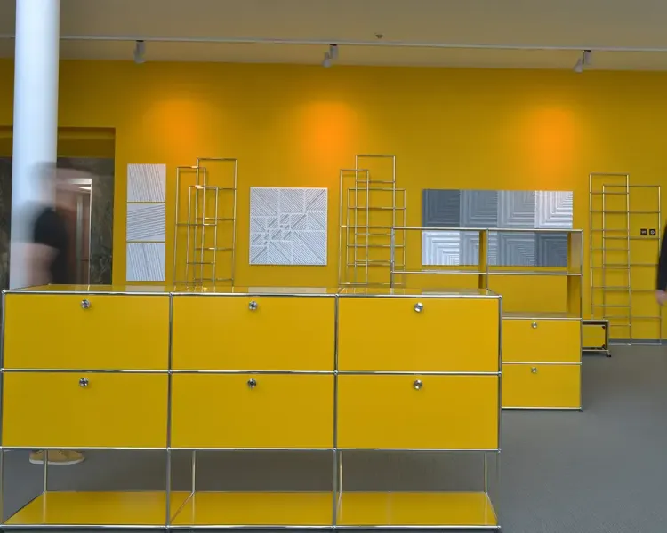Gelbe USM-Haller-Sideboards vor gelber Wand, dahinter weiße Reliefbilder