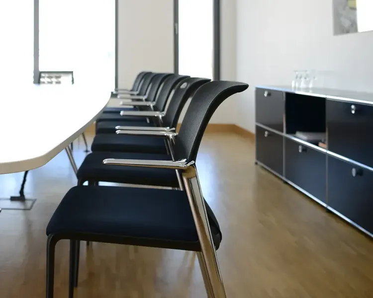 Reihe blauer Konferenzstühle an einem Tisch, dahinter ein Sideboard
