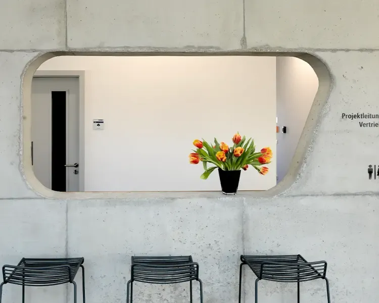 Durchreiche in einer Sichtbetonwand mit Tulpenstrauß, davor Barhocker