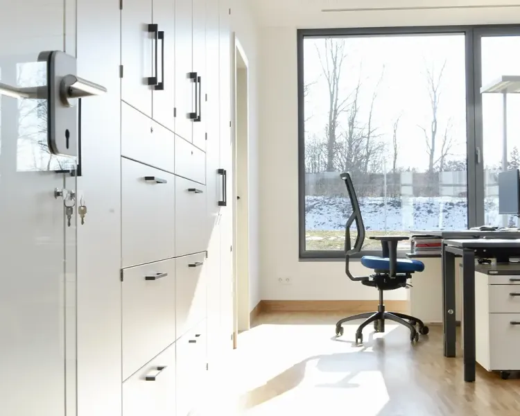 Büro mit weißer Schrankwand, Schreibtisch und Drehstuhl am Fenster
