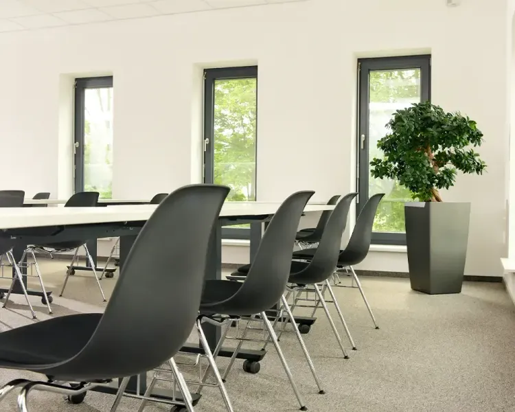 Schulungsraum mit schwarzen Stapelstühlen an langen Tischen