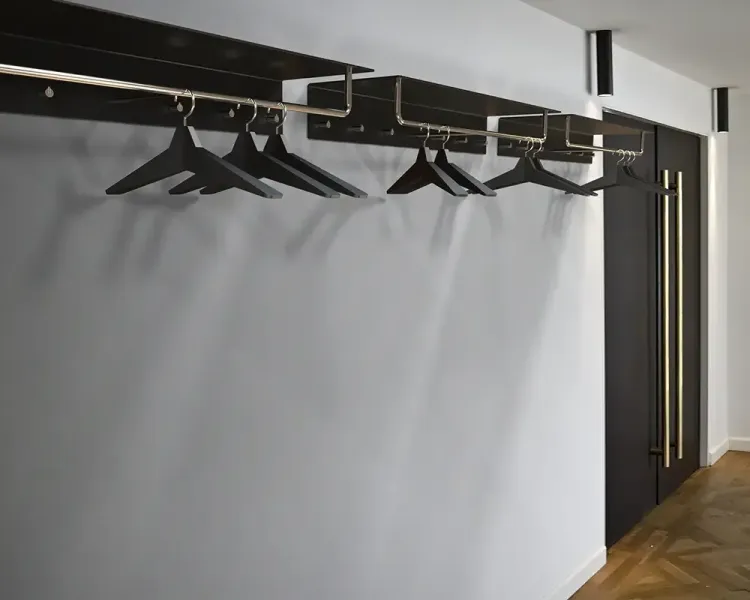 Hängende Garderobenstange mit schwarzen Kleiderbügeln an einer weißen Wand