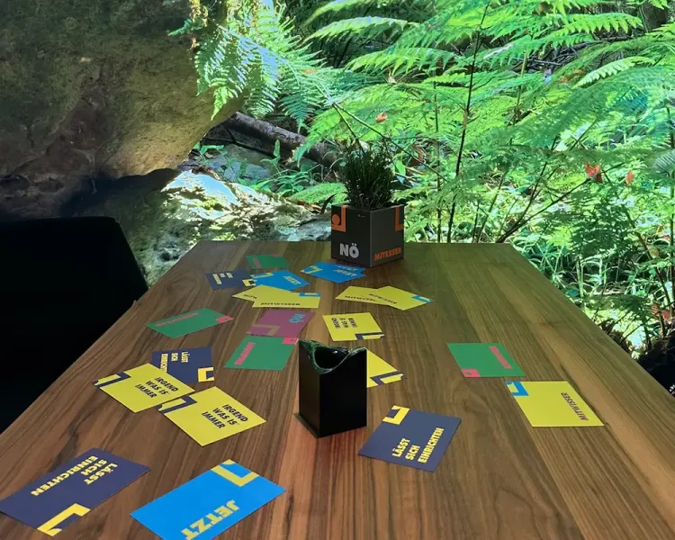 Holztisch mit bunten Spielkarten vor einer Waldtapete