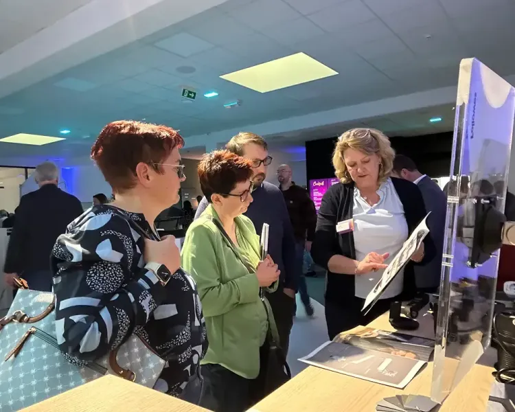 Mitarbeiterin zeigt zwei Besucherinnen Muster an einer Ausstellungsstele