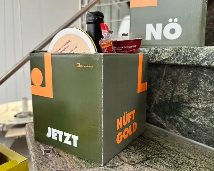 Gefüllte Geschenkbox in Olivgrün mit den Aufschriften „Jetzt“ und „Hüftgold“
