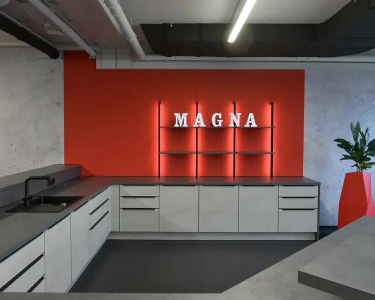 Küchenzeile mit Spüle vor roter Wand mit beleuchtetem Magna-Schriftzug