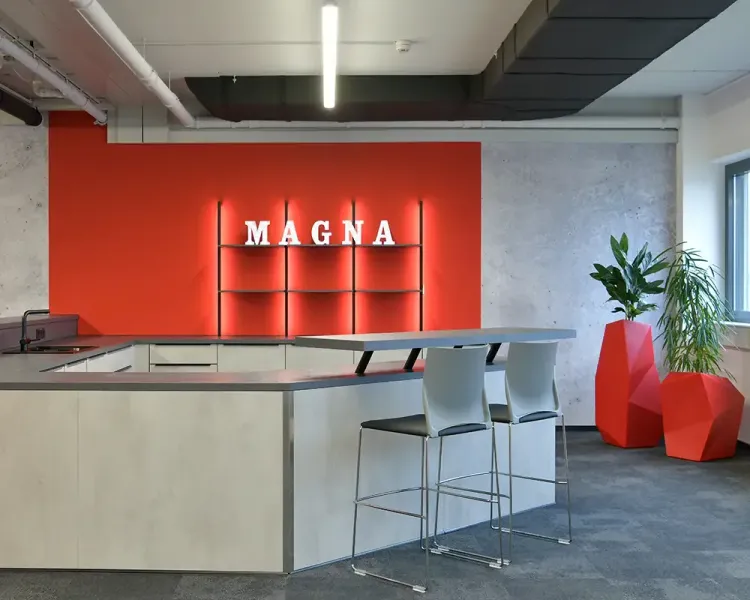 Küchenzeile vor roter Wand mit beleuchtetem Magna-Schriftzug und Barhockern