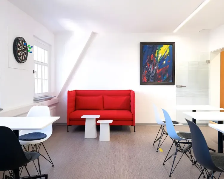 Aufenthaltsraum mit rotem Sofa, Dartscheibe und Kunstwerk an der Wand