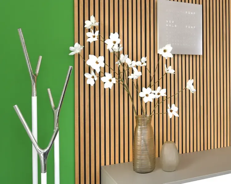 Holzlamellenwand mit Vase, Wortuhr und weißen Blüten vor grüner Wand