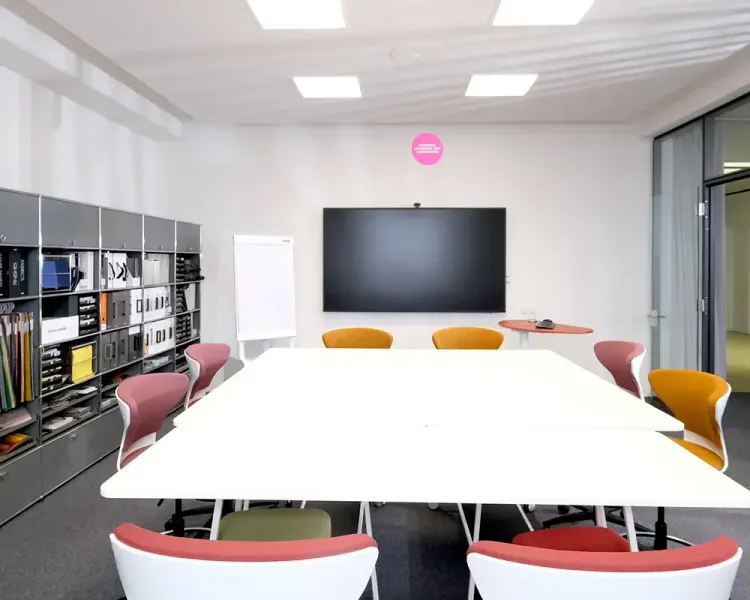 Projektwerkstatt mit weißer Tafel, farbigen Stühlen, Bildschirm und Regalwand