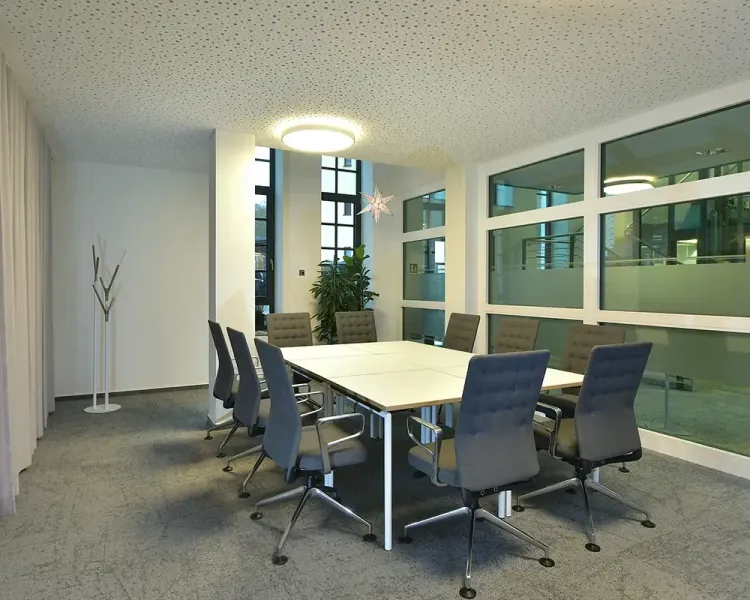 Besprechungsraum mit hellem Tisch, blauen Drehstühlen und Deckenleuchte