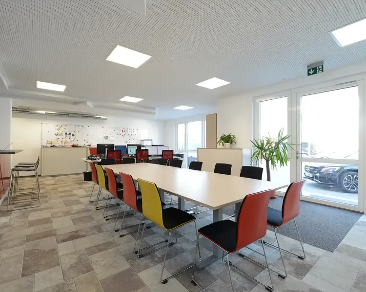 Multifunktionsraum mit langem Tisch, farbigen Stühlen und Whiteboard