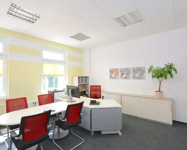 Büro mit rotem Besprechungstisch und Arbeitsplatz vor gelber Wand