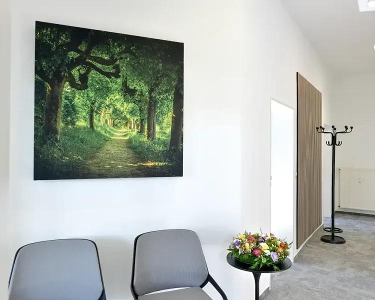 Wartebereich mit Waldbild, zwei Stühlen und Blumenschmuck