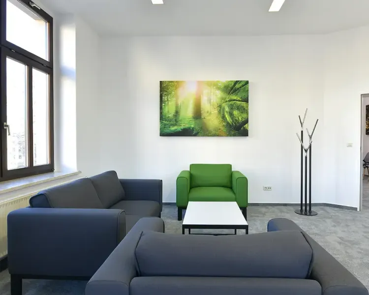 Sitzgruppe mit grauen Sofas und grünem Sessel unter einem Waldbild