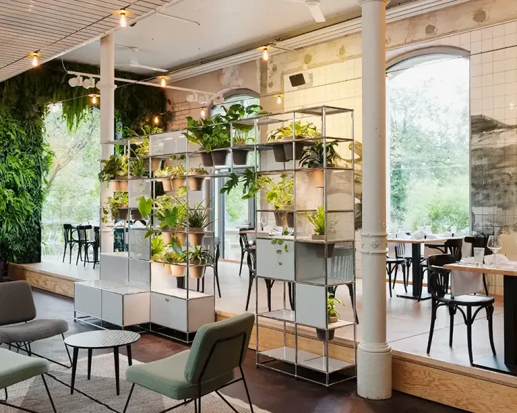 Begrünte Regalsysteme als Raumteiler in einem Café mit Bistrostühlen