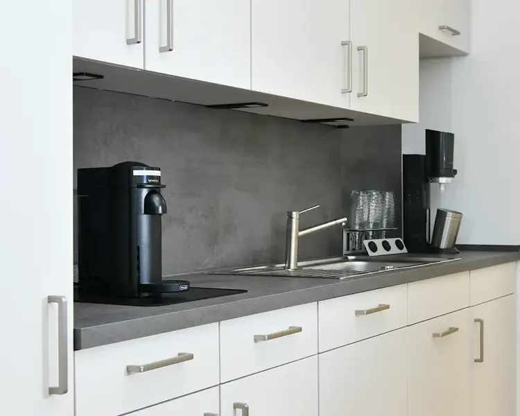Teeküche in Weiß mit dunkler Arbeitsplatte, Kaffeemaschine und Spüle