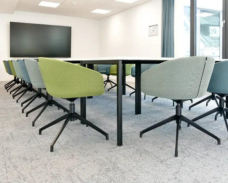 Besprechungsraum mit farbigen Drehsesseln, Bildschirm und Vorhang