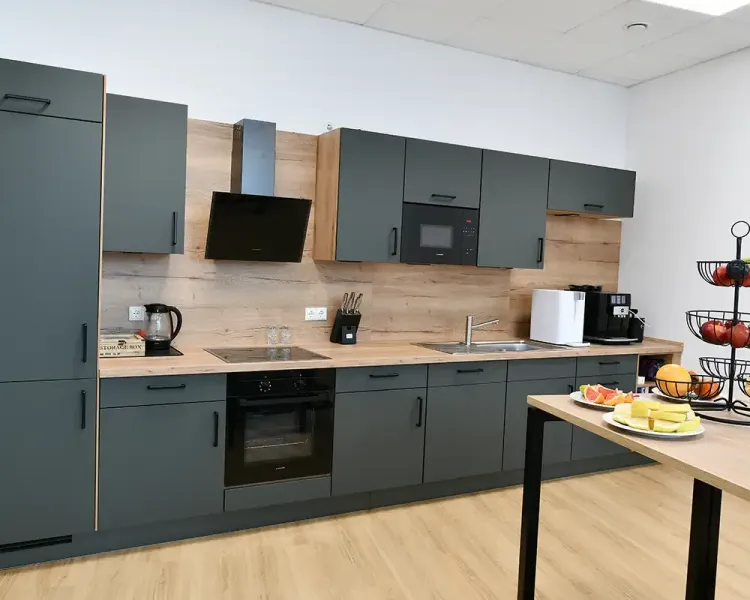 Küchenzeile in Dunkelgrün mit Holzrückwand, daneben ein Tisch mit Obst